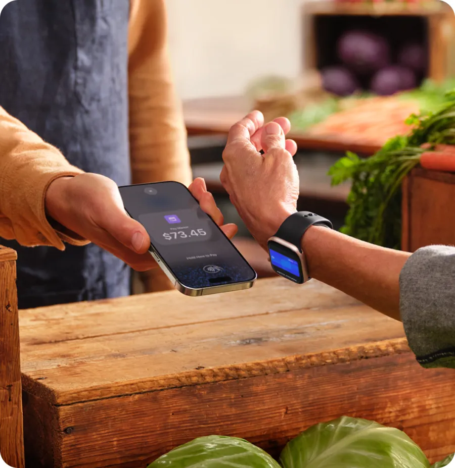 At a market stall, a customer pays with Apple Watch held near the seller’s iPhone.