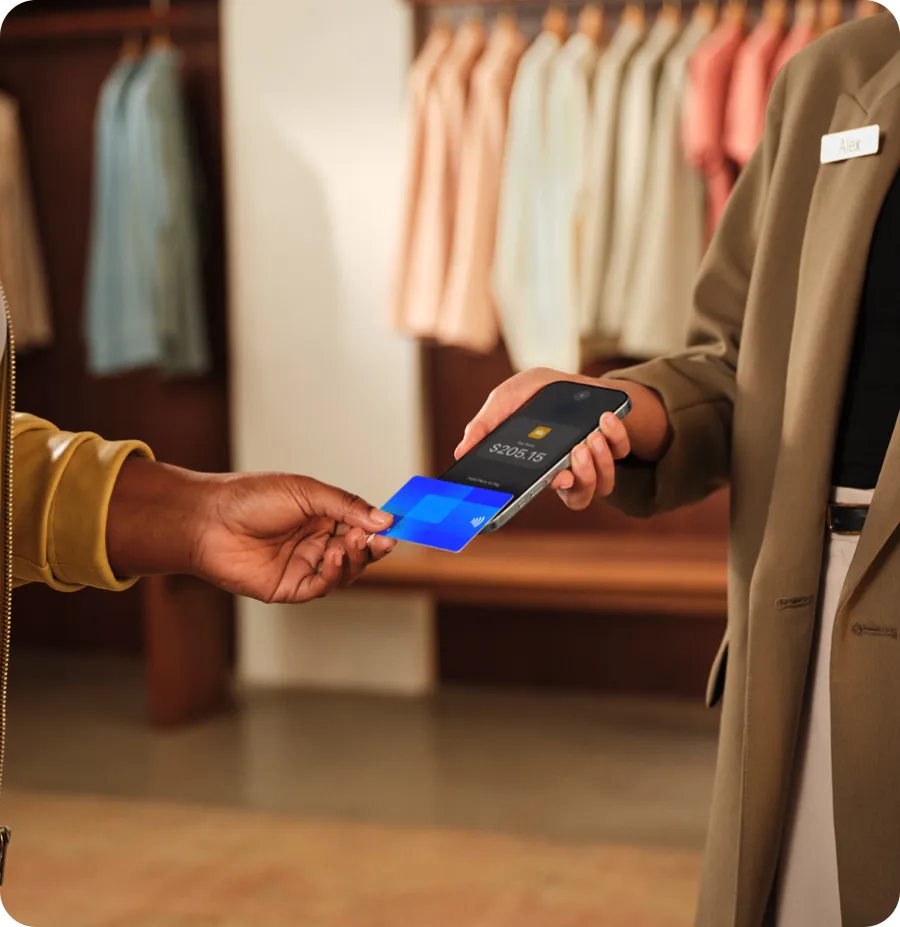 A shop worker holds out an iPhone while a customer taps a card on it.